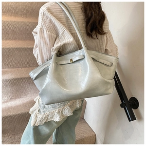 Detail of a high-gloss pleated tote bag with golden lock on a striped shirt model