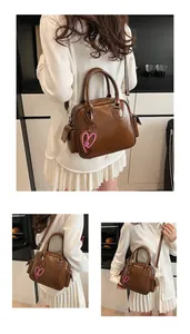 Detail of a brown glossy tote bag with heart charm and adjustable shoulder strap