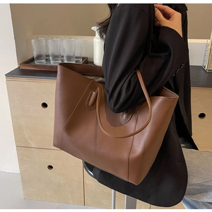 Grand sac cabas en cuir marron porté à l'épaule dans un intérieur de style minimaliste