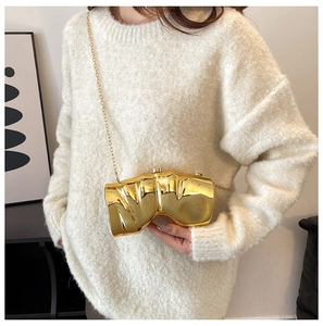 Gros plan d'un sac bandoulière doré métallique avec texture plissée sur pull blanc