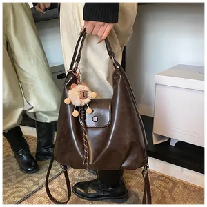Detail of hobo handbag in dark brown faux leather featuring lion plush and braided charm