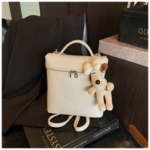 Detail of creamy litchi grain leather backpack with silver zipper and cute plush puppy charm