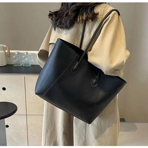 Vue latérale d'un grand sac cabas en cuir noir mat porté par un mannequin en décor épuré