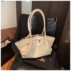 Close-up of cream pleated tote bag with matte gold buckle on a stylish black leather chair