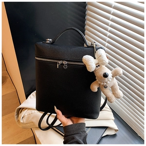 Close-up of black lychee grain leather backpack with silver zippers and plush dog charm