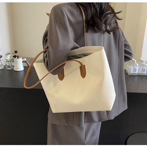 Grand sac cabas en cuir crème avec anses marron porté par un mannequin dans un café