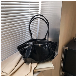 Detail of a black glossy patent leather tote bag with a gold rectangular buckle and long straps