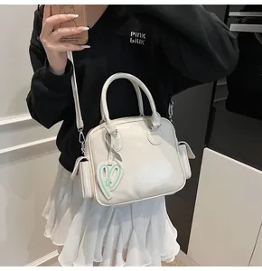Close-up of white PU leather bowling bag with top handle and green heart charm detail