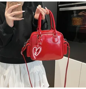 Detail of red glossy leather tote bag with heart charm and matching shoulder strap