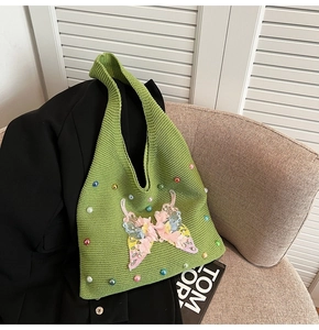 Détail d'un sac cabas en tricot vert orné de perles et d'un papillon brodé