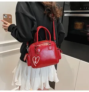 Detail of red Boston bag with shiny finish, top handle, and heart tag on a model