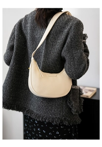 Nahaufnahme der cremeweißen Halbmond-Tasche aus Leder mit Lychee-Muster am Model