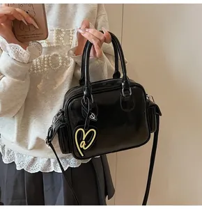 Detail of black glossy tote bag with heart charm and side flap pocket for women
