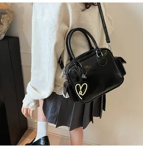 Detail of black glossy faux leather Boston bag with side pockets and heart charm