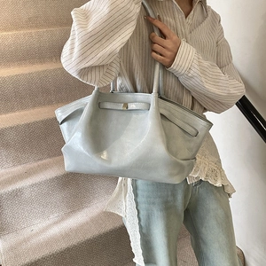 Light blue pleated tote bag made of glossy leather shown on shoulder in indoor setting