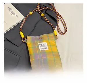 Detail of plaid crossbody bag with vibrant braided strap and purple tassel charm