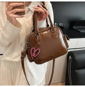 Detail of a dark brown patent leather tote bag with a pink heart pendant and dual handles