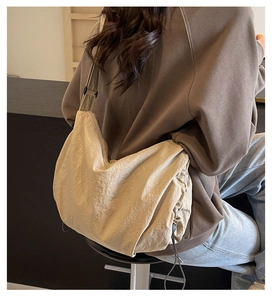 Detail of the oversized beige nylon shoulder bag showing pleated texture and drawstring base
