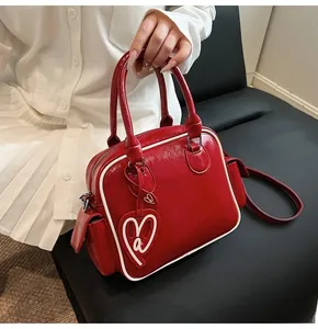 Detail of red glossy leather tote bag with white piping and heart shape charm accessory