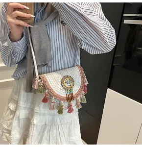 Detail of straw woven crossbody bag with colorful tassels and bohemian beaded badge