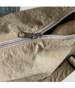 Detail of silver metallic zipper and crinkled nylon fabric on khaki crossbody bag