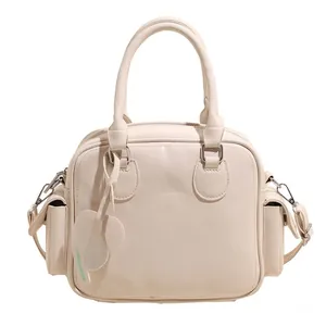 Detail of a cream faux leather tote bag with side pockets and a green heart charm