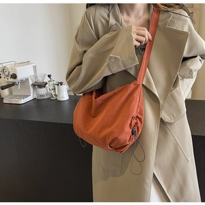 Detailed view of burnt orange nylon shoulder bag with adjustable side drawstring detail