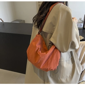 Detailed view of an orange pleated nylon shoulder bag worn over a beige trench coat