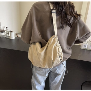 Detail of a beige drawstring crossbody bag with pleated nylon fabric on a female model