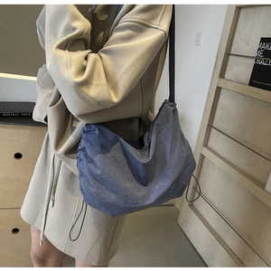 Detail of grey-blue crescent bag with adjustable drawstring side and wide shoulder strap