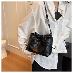 Detail view of a black pleated bucket bag with bow accents and a metal chain strap