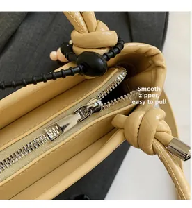 Detailed close-up of smooth silver zipper and knotted shoulder strap on cream bucket bag