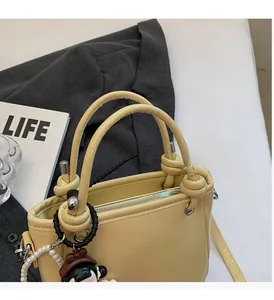 Detail of a beige bucket bag with knotted handle and decorative pearl charm