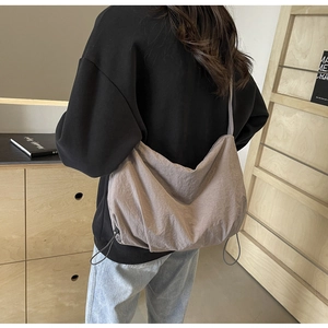 Detail of large brown-gray nylon shoulder bag with drawstring accents on a model