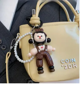 Detail of cartoon doll charm with brown overalls and pearl chain on a beige handbag