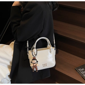Weiße Eimertasche mit Metall-Logo und Anhänger getragen auf einer Außentreppe