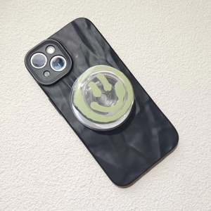 Detail of a black ripple texture phone case with a green smiley face expanding socket grip