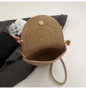 Detail of straw woven bag showing metal magnetic buckle, fringe tassel and natural fiber texture