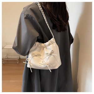 Close-up of pleated cream handbag featuring delicate ribbon bows and silver chain strap