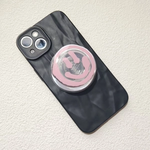 Detail view of black wavy texture phone case with pink smiley face pop socket on white surface