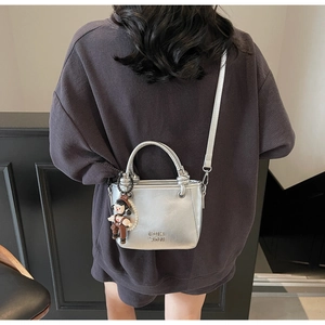 Detailansicht der silbernen Metallic-Eimertasche mit süßem Anhänger und Logo-Prägung