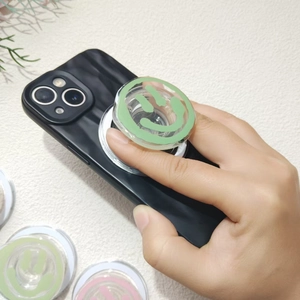 Transparent acrylic mint green smiley face phone grip holder on a black smartphone