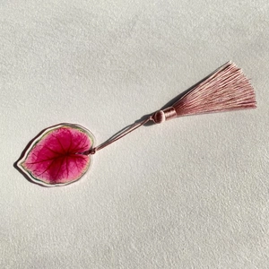 Macro shot of translucent acrylic leaf bookmark with vivid pink veins and silky tassel