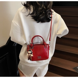 Detail of red patent leather bucket bag with metal logo and cute doll pendant
