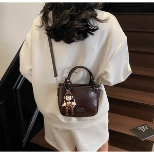 Detail der dunkelbraunen Ölwachs-Leder-Eimertasche mit süßem Cartoon-Puppenanhänger