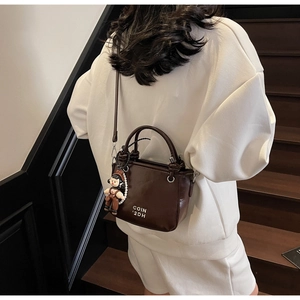 Brown bucket bag side view with long shoulder strap and pearl doll charm detail