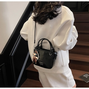 Detail of black glossy bucket bag with pearl chain charm and metal letters on stairs