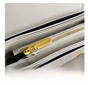 Detailed close-up of the smooth gold metal zipper on a white leather shoulder bag