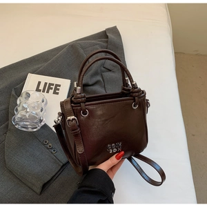 Detail einer dunkelbraunen, glänzenden Eimertasche mit silbernem Logo und Tragegriff