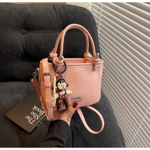 Detail der rosa Bucket Bag aus Ölwachsleder mit Perlenanhänger und Metalllogo auf Sofa
